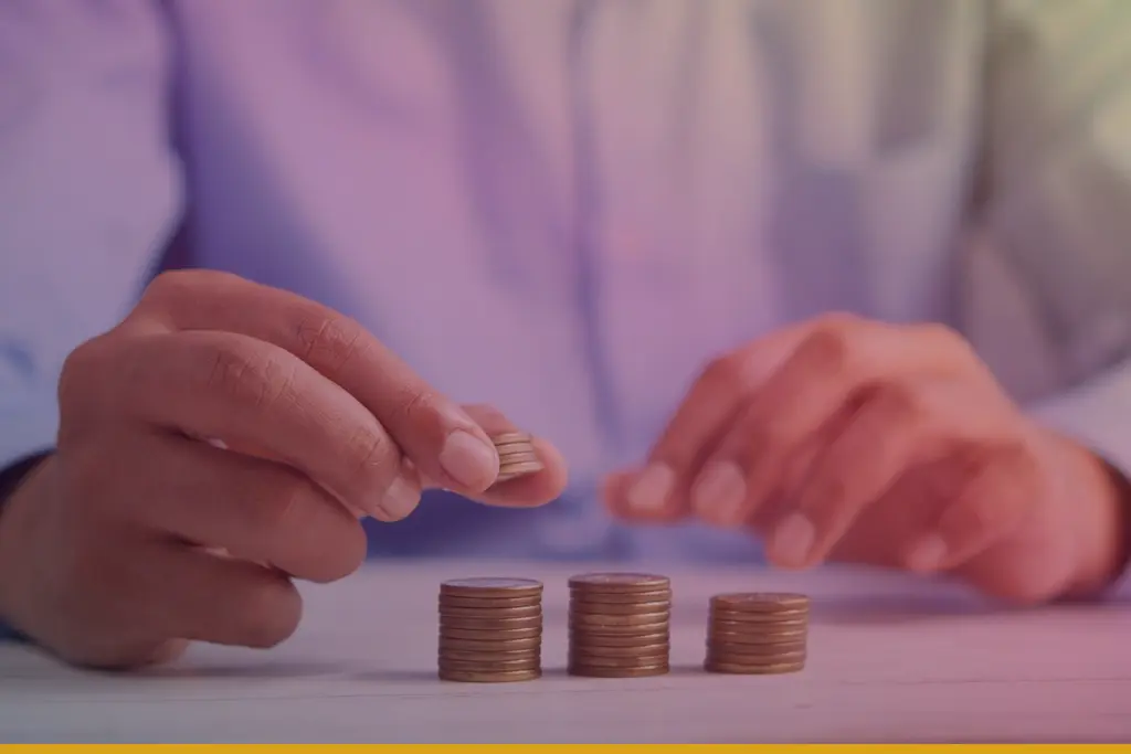 Persona con camisa azul apilando monedas sobre una mesa de madera clara